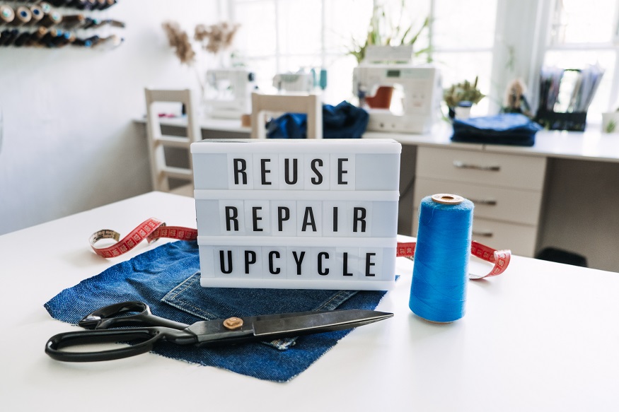 EPR für Alttextilien, Reuse, repair, upcycle text on light board on sewing machines background. Stack of old jeans, Denim clothes, scissors, thread and sewing tools in sewing studio. Denim Upcycling Ideas, Using Old Jeans